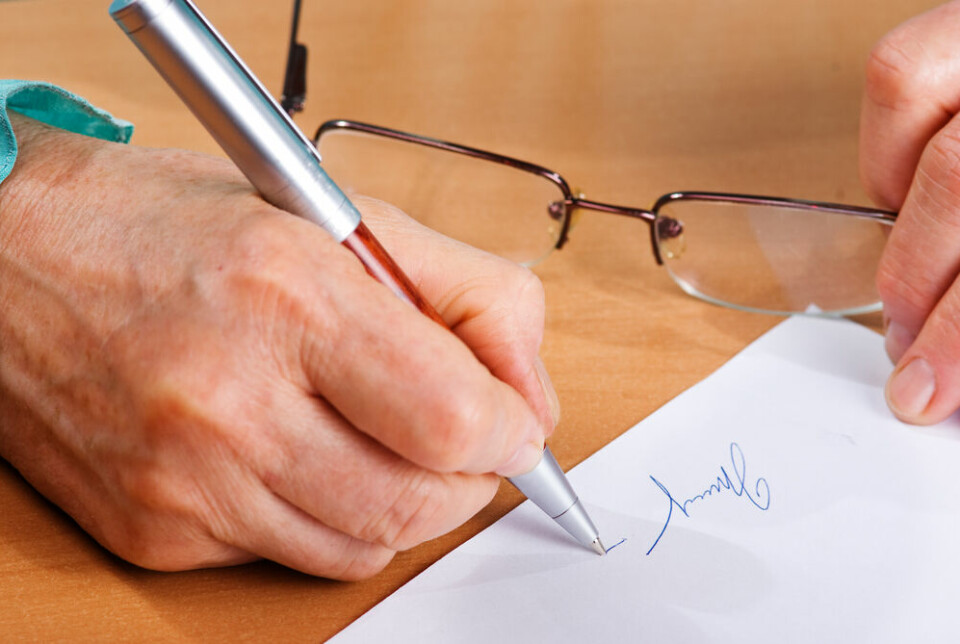 A view of an older woman signing a piece of paper