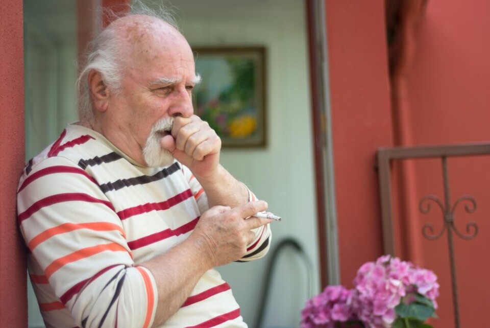 An older man smoking outside and coughing