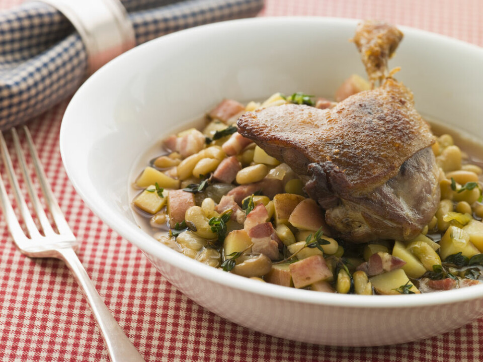 A view of a confit duck leg served with traditional beans and bacon