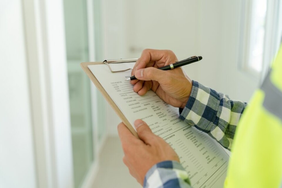 A view of a man with a high-vis jacket on, writing on a form on a clipboard, in a house