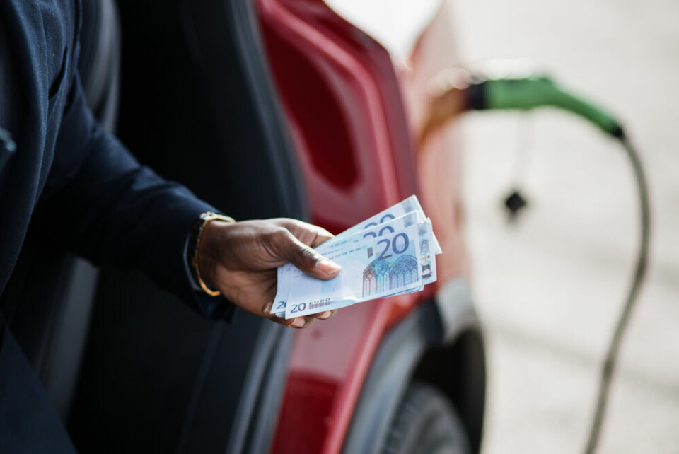 A view of a man holding some euros with an electric car charging in the background