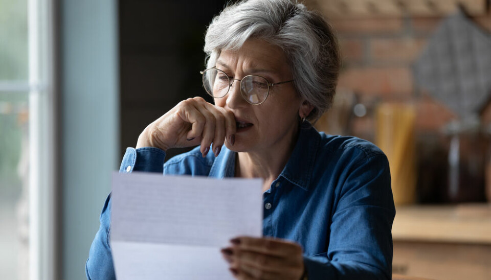 An elderly woman in her French home looking at a bill or document.
