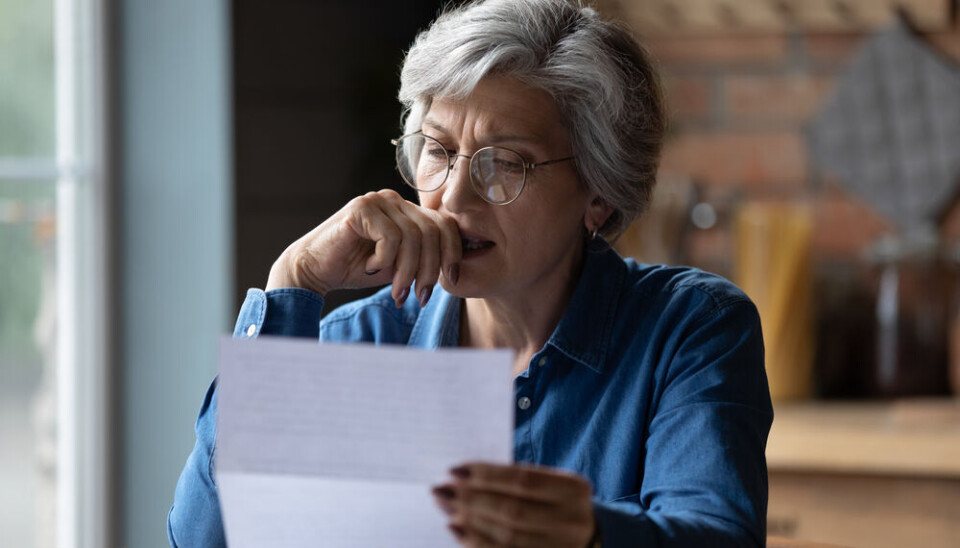 An elderly woman in her French home looking at a bill or document.