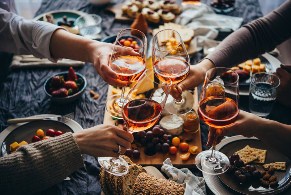 fornStudio/Shutterstock. Four people clinking glasses of rosé wine at a dinner table
