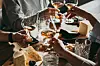 People clinking wine glasses over a cheeseboard