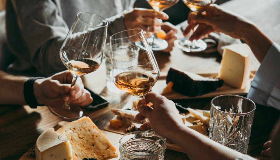 People clinking wine glasses over a cheeseboard