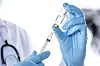 A doctor wearing gloves preparing a syringe with a vaccine liquid from a vial
