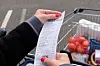 A view of a woman holding a supermarket receipt with her full shopping trolley in the background
