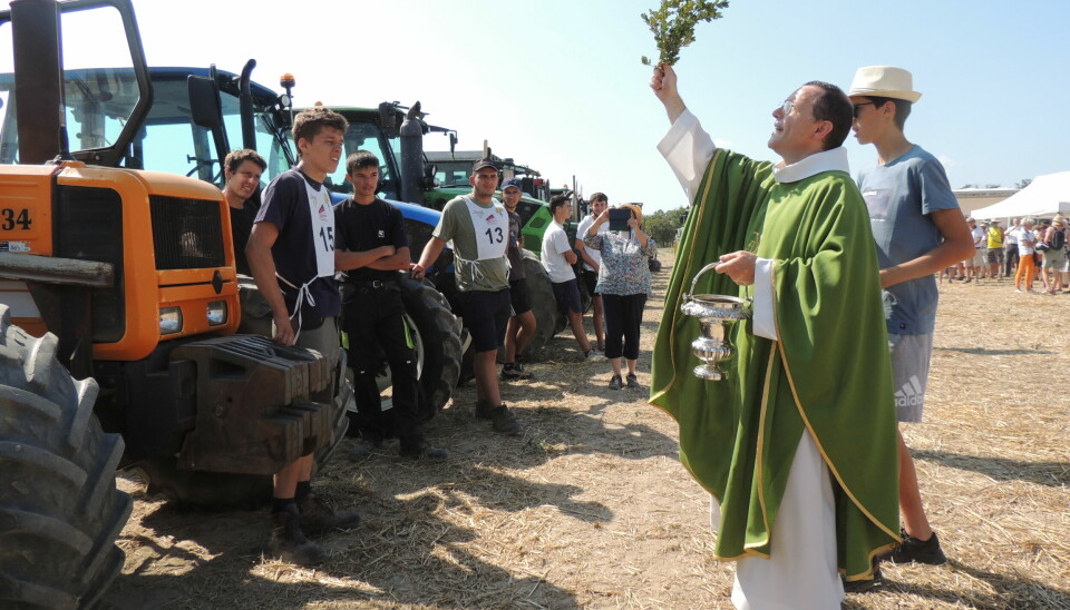 French priest blesses a line of tractors under blue sky