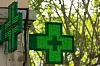 A view of a green light-up pharmacy cross sign against green trees