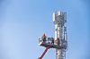 Engineers attach antenna high up 5G mast against blue sky in Normandy, France