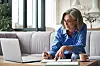 An old person looking at her computer and making notes