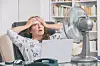 A woman working in an office during a heatwave. She is sitting in front of a fan.