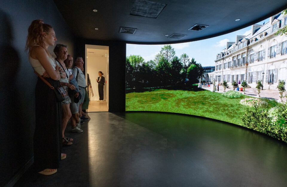 X.com/Elysee / Maison Elysée Une vue de personnes regardant un film dans l'exposition de la Maison Elysée