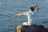 Man sitting on a rock throws a bottle out to sea
