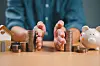 A view of a man separating piles of coins, with a piggy bank and house to show debts