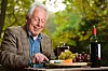 An old man eats cheese and drinks wine