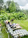 A woman sits in a wooden deck chair in her garden with two dogs