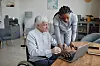 A carer helps an elderly man on his laptop