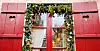 A window framed by red shutters decorated with a garland
