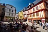 People sit at café tables in a sunny square surrounded by colourful half-timbered houses in Vannes, France.