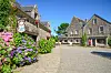 Cobbled square in Locronan with stone houses, flowers and a clear blue sky.