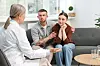Man and woman sit on a sofa facing a health professional