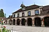 Arcaded town hall with clock tower and hanging flowers in a sunny village square.