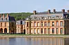 Classical French château reflected in a still ornamental lake on a sunny day.