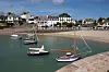 Small sailing boats moored in a calm harbour below white houses and a sandy beach in Locquirec, Brittany.