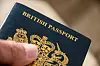 Close-up of a hand holding a British passport with gold crest on the cover.