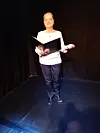 Person on dark stage holding an open folder while rehearsing.