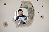Worker using a power drill to demolish an interior wall seen through a hole