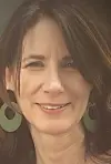 Close-up of a smiling woman with long dark hair and green earrings.