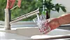 Male hands filling a clear glass with tap water from a stainless steel kitchen tap