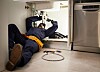 Plumber on the kitchen floor repairing pipes beneath a sink unit