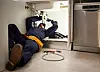 Plumber on the kitchen floor repairing pipes beneath a sink unit