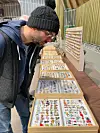 Person looking closely at trays of miniature figurines on a market table