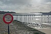 French warning sign by a cobbled shore with a raised walkway over the bay at low tide