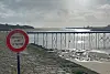 French warning sign by a cobbled shore with a raised walkway over the bay at low tide