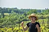 Person in straw hat talking in a sunny vineyard with green hills behind