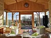 Sunlit wooden lounge with armchairs facing open doors to a terrace and trees