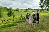 Group of people on a grassy hill overlooking green vineyards and farm buildings