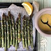 Roasted asparagus on a lined tray with grated cheese, lemon wedge and bowl of sauce.
