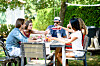 Group of friends raising drinks at a picnic table in a sunny garden