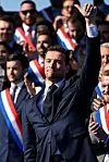 Jordan Bardella raises his arm at a rally, amid supporters in tricolour sashes