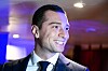 Jordan Bardella smiling in a suit at an indoor launch event