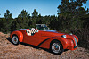 Red vintage-style convertible car parked on a gravel roadside near pine trees