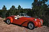 Red vintage-style convertible car parked on a gravel roadside near pine trees
