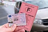 Hand holding a pink French paper driving licence beside a modern plastic licence card near a parked car.